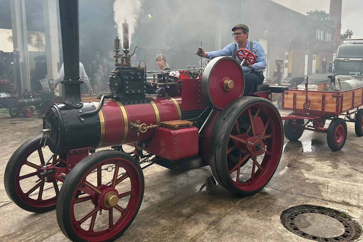Ein Dampftraktor als Modell in der Farbe rot fährt auf einer Straße