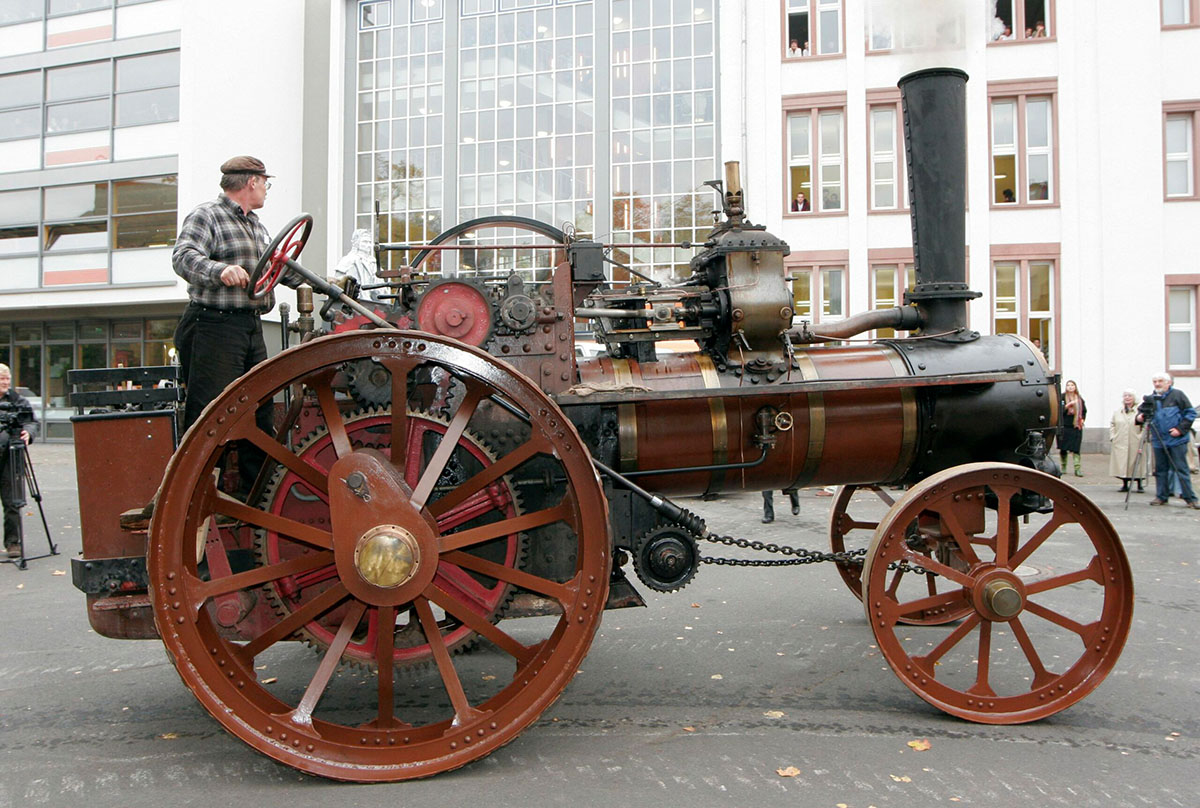 Ein Dampftraktor, Typ D5 mit Baujahr 1896 steht auf einem Platz in einer Stadt.