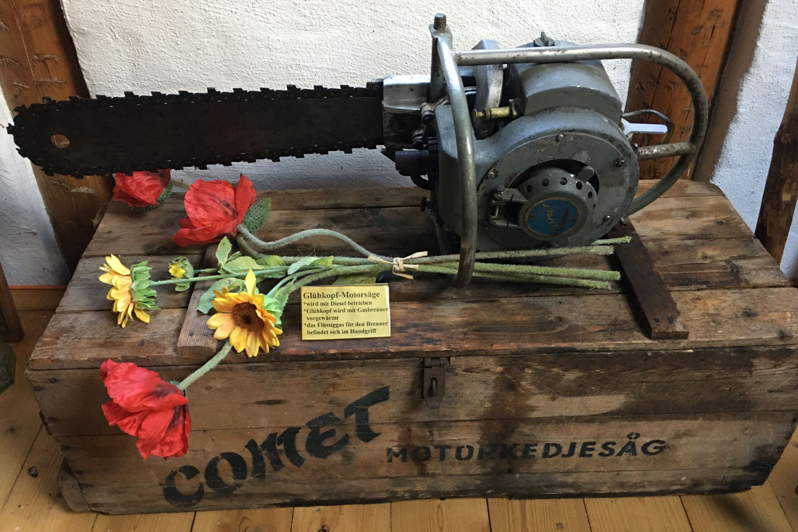 Eine historische Glühkopf-Motorsäge auf einer Holzkiste dekoriert.