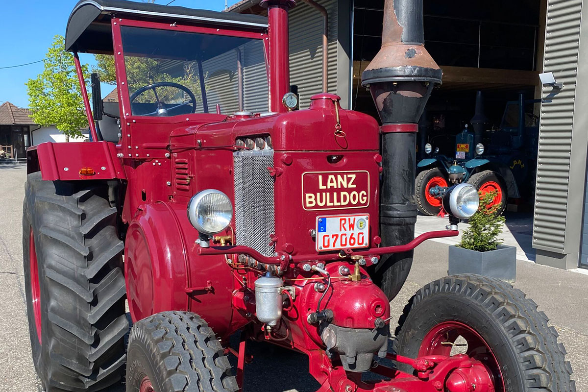 Ein roter Lanz D9506 steht auf dem Hof vor einer Scheune.