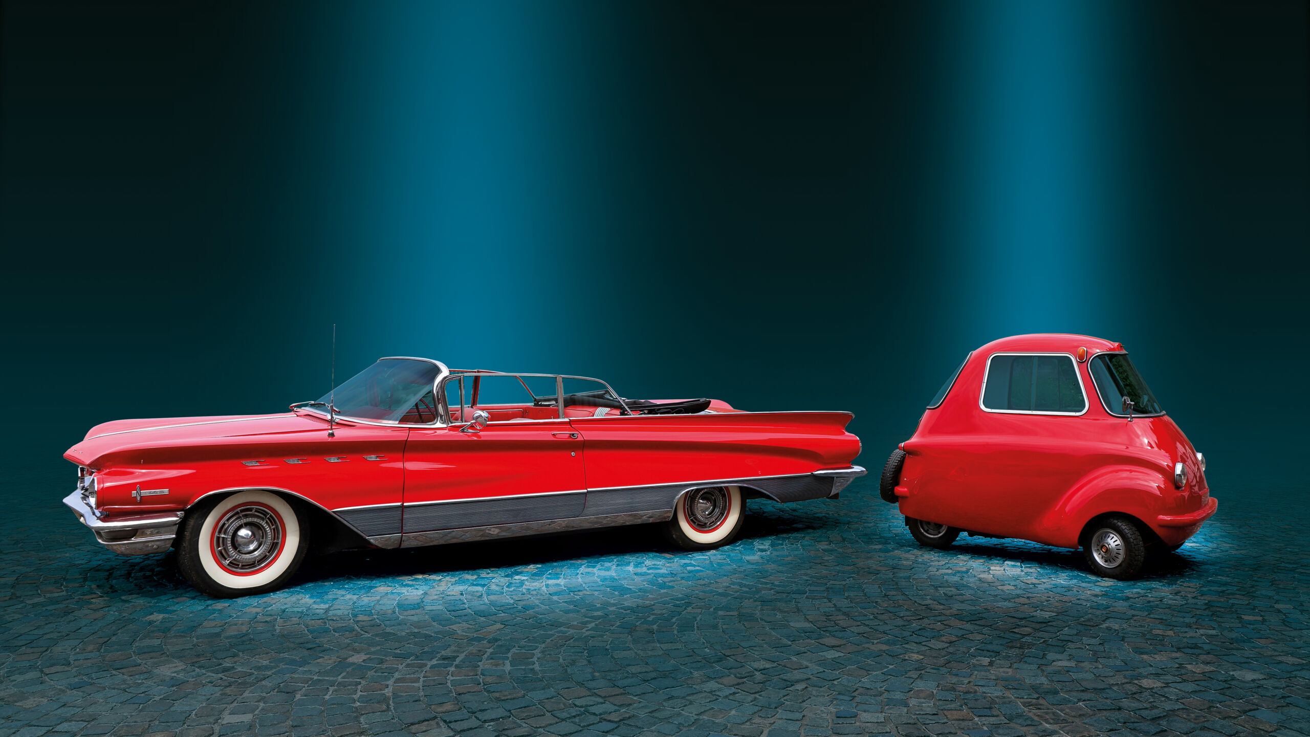 Ein großer US-Car und ein kleiner Scoota-Car stehen nebeneinander. Beide Fahrzeuge sind rot.