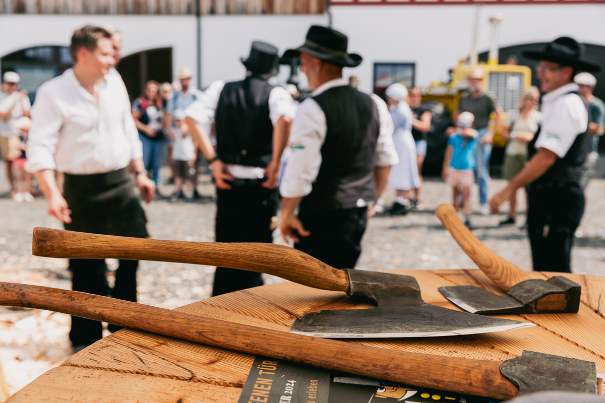 Verschiese Äxte liegen auf einem Tisch. Im Hintergrund stehen Zimmermänner